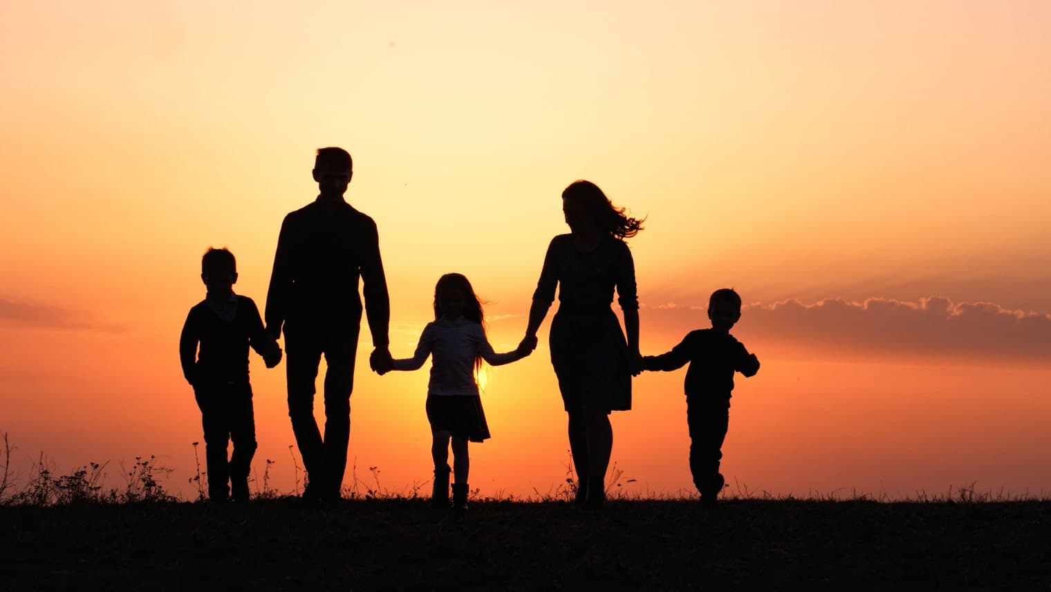 A family holding hands walking into a sunset